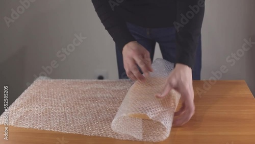 Close-up of a man's hands covering a plastic box with an air bubble wrap at a table in a warehouse