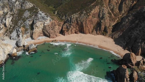 Drone footage of remote beach with its wide sandy coast. Stormy sea washing wild and unspoiled cliffs with natural beauty around. Europe, Portugal, Sintra, Ursa Beach. High quality 4k footage