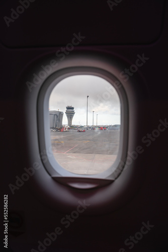 views from the plane overlooking the runway with its boarding bridge and control tower. It is a very gray day.