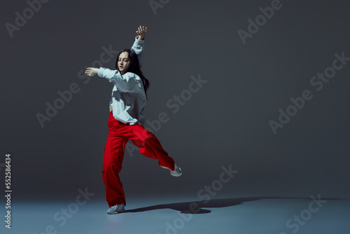 Energetic young girl dancing contemporary dance isolated on dark grey background with shadow. Experimental dance. Music, dance, active lifestyle, fashion, style