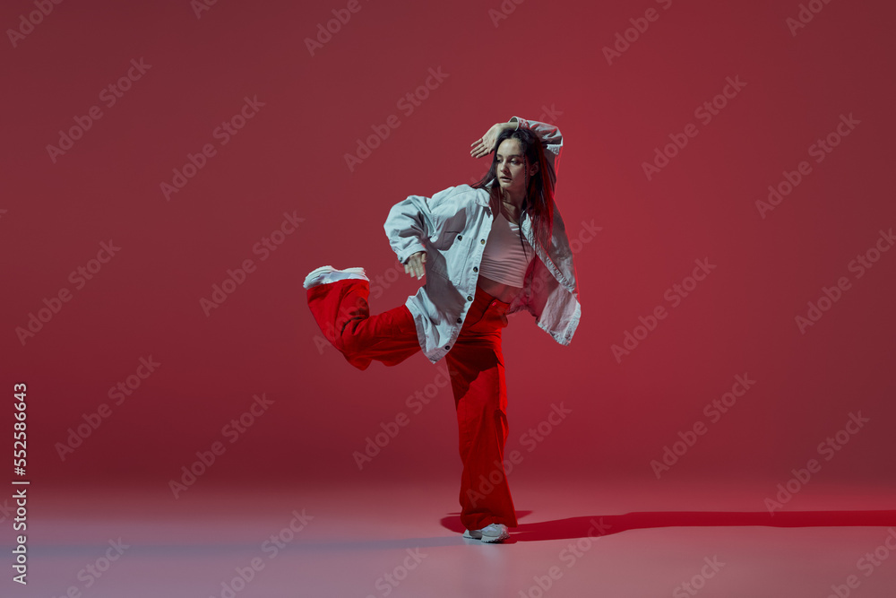 Dynamic portrait of young girl dancing hip-hop or contemporary dance isolated on dark red background. Experimental dance. Music, dance, active lifestyle, fashion, style Dynamic portrait of young girl dancing hip-hop or contemporary dance isolated on dark red background. Experimental dance. Music, dance, active lifestyle, fashion, style