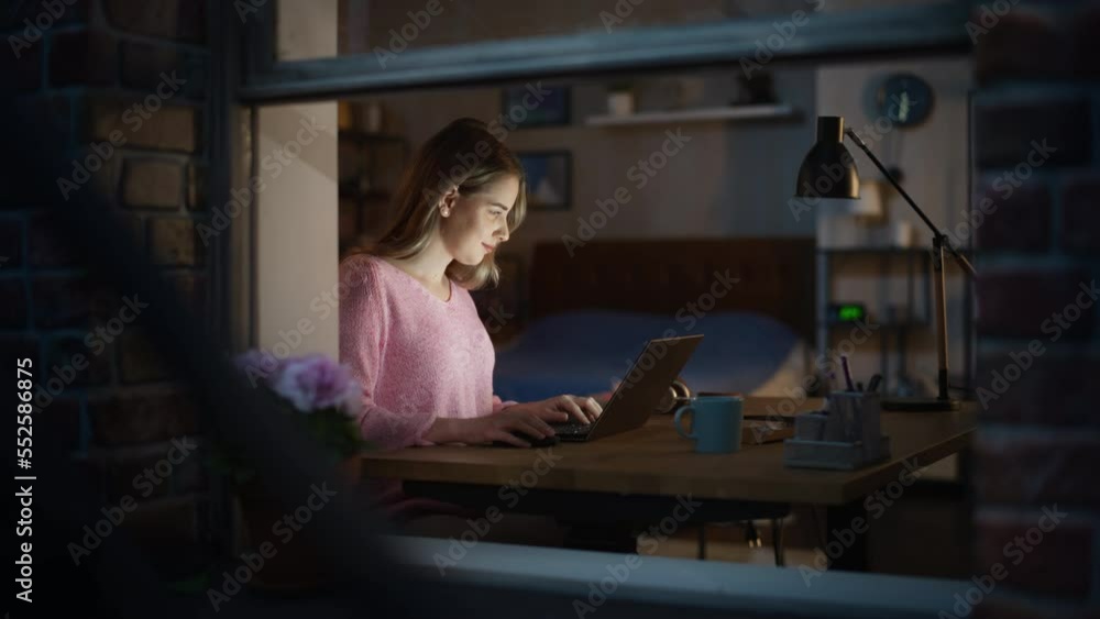 Working from Home Concept: Creative Female Designer Using Laptop, Thinking and Creating New Visual Concept for Online Marketing Campaign. Night Shot, Viewed Through a Window from Outside Working from Home Concept: Creative Female Designer Using Laptop, Thinking and Creating New Visual Concept for Online Marketing Campaign. Night Shot, Viewed Through a Window from Outside
