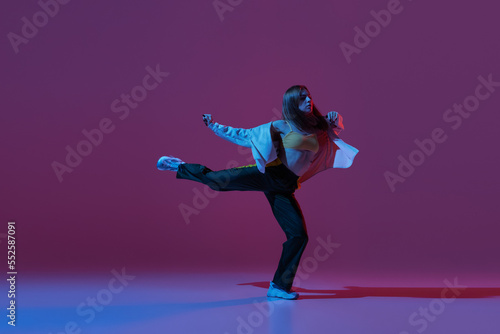 Flexible young girl, contemp dancer dancing hip-hop or experimental dance isolated on dark purple background in neon. Contemporary dance. Music, dance, active lifestyle, fashion, style photo