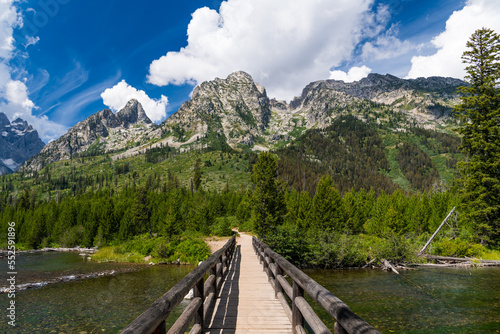 Hiking trail bridge crossing a wide river towards high, rugged mountain peaks in Grand Teton National Park