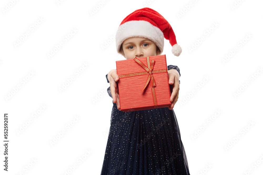 Selective focus on a stylish red gift box in the hands of a cute baby girl, holding out a Christmas present on camera, isolated on white background. Boxing Day. Xmas and New Year's celebration concept Selective focus on a stylish red gift box in the hands of a cute baby girl, holding out a Christmas present on camera, isolated on white background. Boxing Day. Xmas and New Year's celebration concept