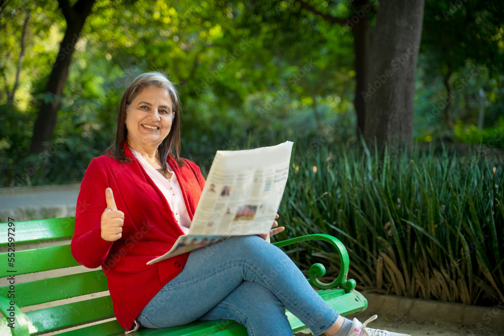 Obraz premium Senior Indian woman reading newspaper at park.