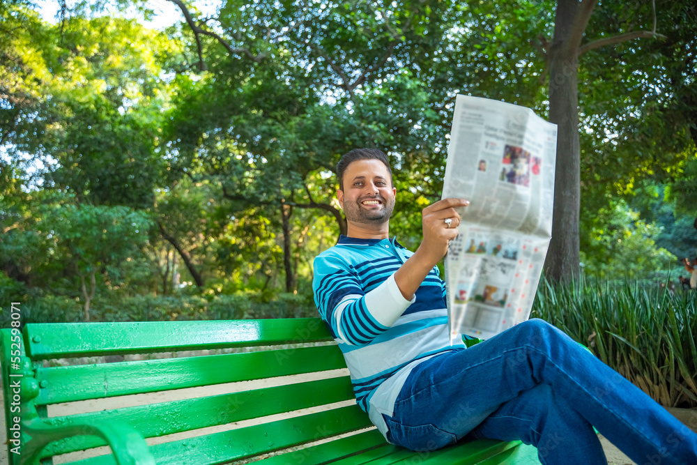 Young indian man reading news paper at park. Young indian man reading news paper at park.