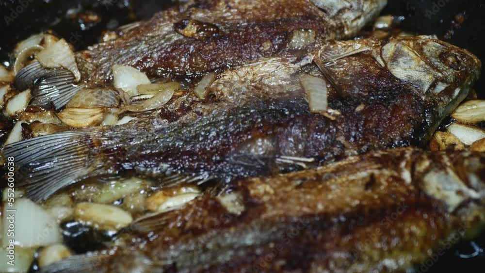 appetizing freshwater fish with crust and onion fry in a frying pan, close-up appetizing freshwater fish with crust and onion fry in a frying pan, close-up