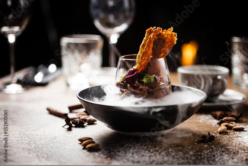 Chocolate mousse with coffee liquor, cherry, kama biscuit in liquid ice smoke in a bowl. Delicious healthy food closeup served for lunch on a table in modern gourmet cuisine restaurant