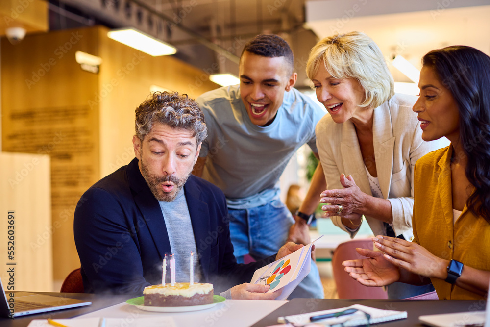 Staff Celebrating Birthday Of Male Colleague At Desk In Office With Cake And Card Staff Celebrating Birthday Of Male Colleague At Desk In Office With Cake And Card