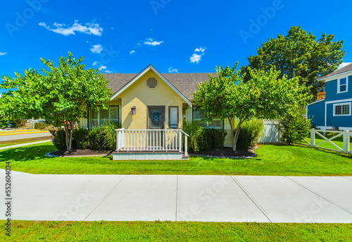 Fotografie Small yellow family house on sunny day with green lawn and concrete pathway