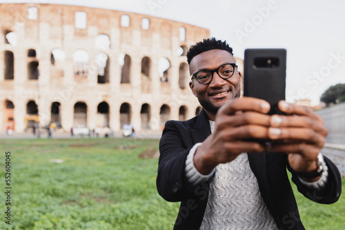 Photography an African boy visiting the coliseum takes a selfi, smiling with the phone in hi