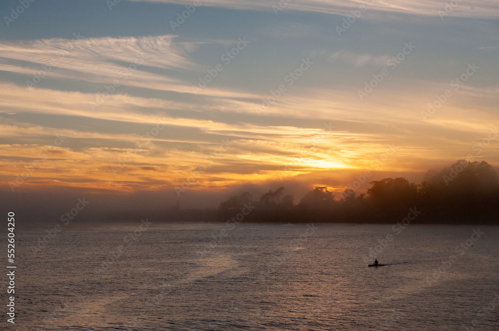 Silhoutte of a person in a kayak peddling in the Santa Cruz bay during sunset.