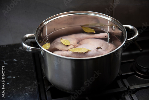 Surowe mięso z kurczaka w wodzie z ziołami w stalowym garnku na czarnej kuchence gazowej