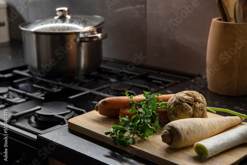 Warzywa na rosół i duży stalowy garnek na kuchence gazowej w tle