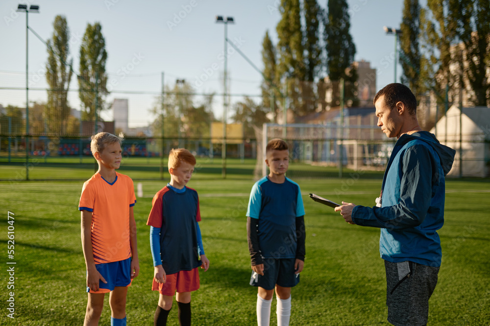 Fototapeta premium Young soccer coach teaching kids on football field
