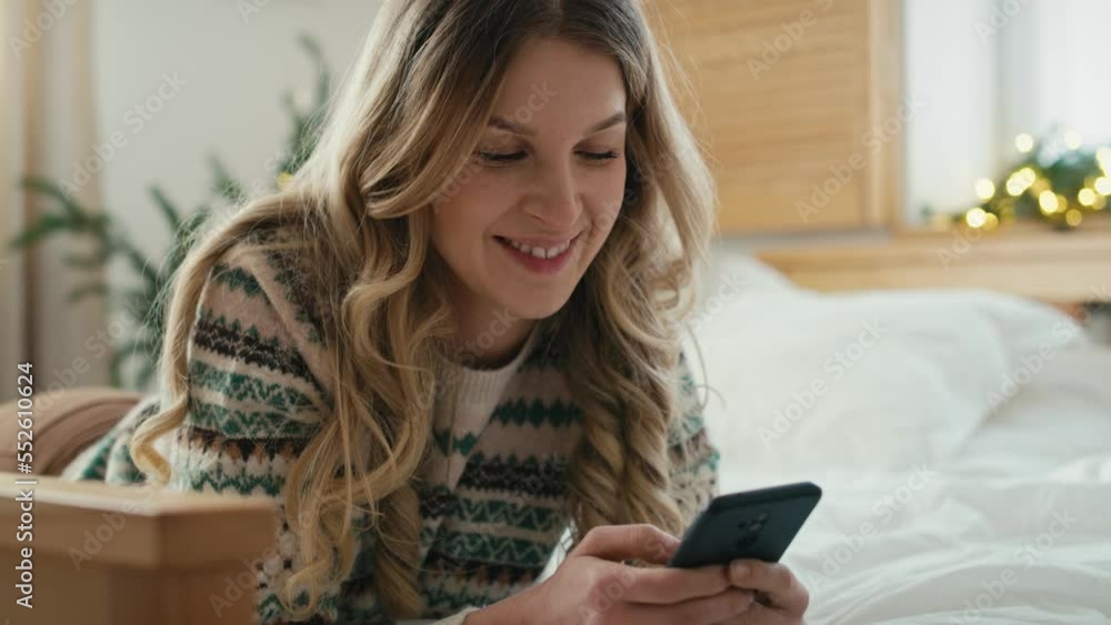 Caucasian woman using phone while lying down on front in bed on Christmas time. Shot with RED helium camera in 8K. Caucasian woman using phone while lying down on front in bed on Christmas time. Shot with RED helium camera in 8K.