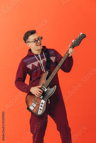 A young man in a Christmas kigurumi plays an electric guitar on a colored background.