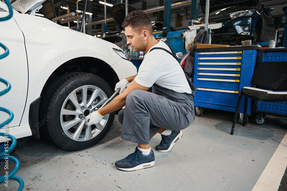 Handsome male changing car wheel in tire fitting Handsome male changing car wheel in tire fitting