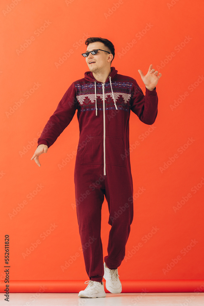 A young man in sunglasses and a Christmas kigurumi dances on a red background. A young man in sunglasses and a Christmas kigurumi dances on a red background.
