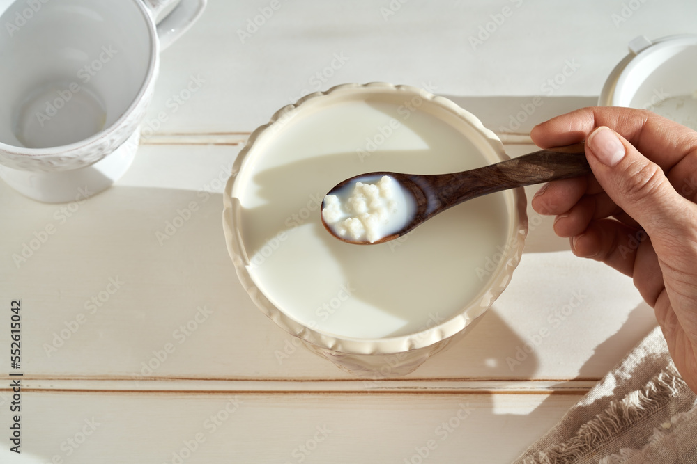 Fresh kefir grains on a wooden spoon above a bowl of milk