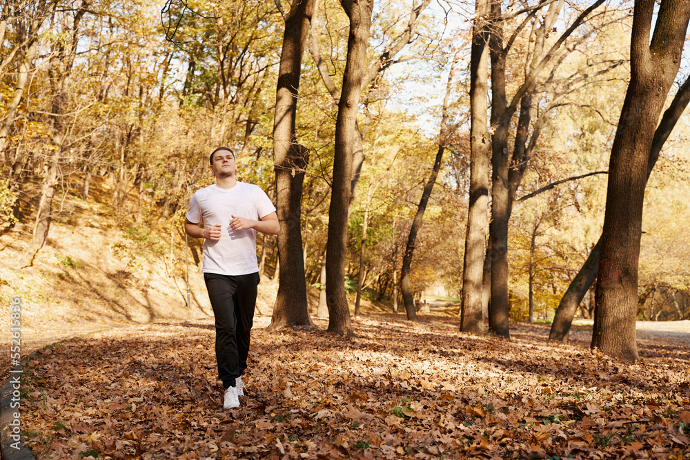 Athletic guy runs along the park alley Athletic guy runs along the park alley