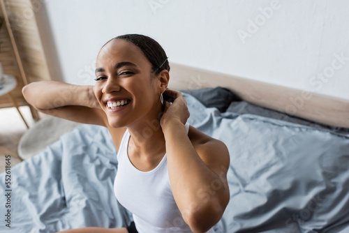 high angle view of positive african american woman smiling and looking at camera in bedroom.