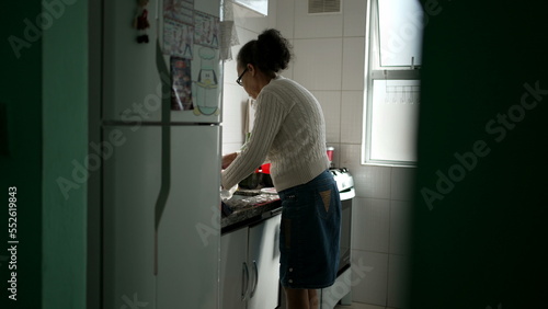 South American senior woman standing at kitchen sink. An older hispanic lady doing housework washing dishes