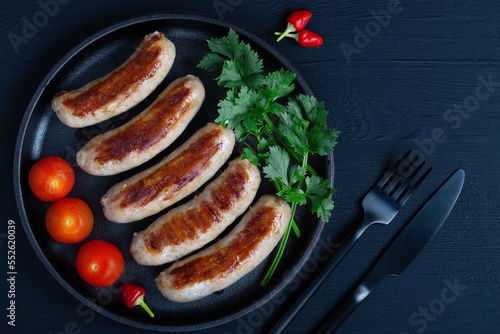 Grilled sausages on pan with herbs and tomato, wood background, closeup