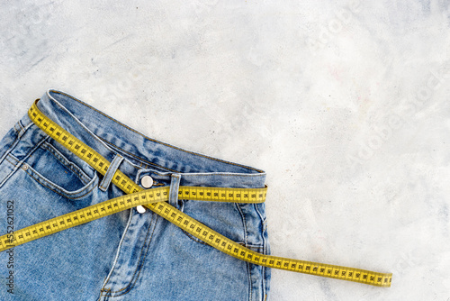 Weight loss concept. Jeans with yellow measuring tape instead of a belt