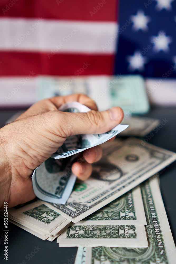 Close-up of a man's hand holding an amount of dollars, with a United States flag in the background. Close-up of a man's hand holding an amount of dollars, with a United States flag in the background.