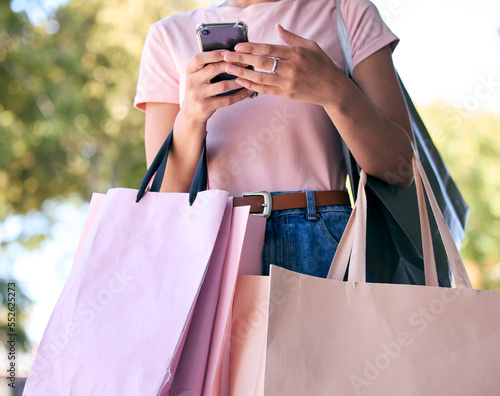 Hands, phone and shopping bags with a woman customer outdoor in a park during summer for consumerism. Ecommerce, online shopping and retail with a female consumer using the internet to search a sale