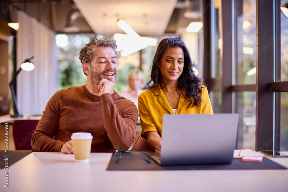 Male And Female Business Colleagues Meeting Around Laptop In Modern Office Male And Female Business Colleagues Meeting Around Laptop In Modern Office