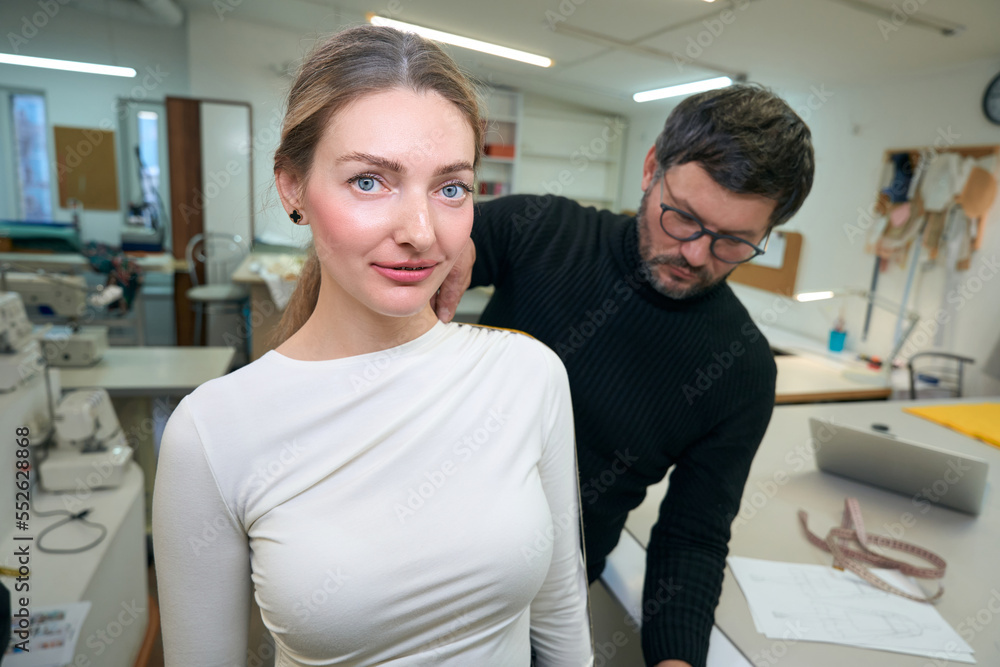Fototapeta premium Male designer in a sewing studio takes measurements from woman