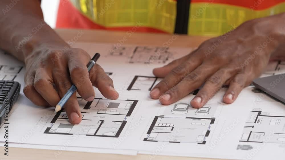 Engineering and construction managers discussing project blueprint on the table at construction site. Engineering and construction managers discussing project blueprint on the table at construction site.