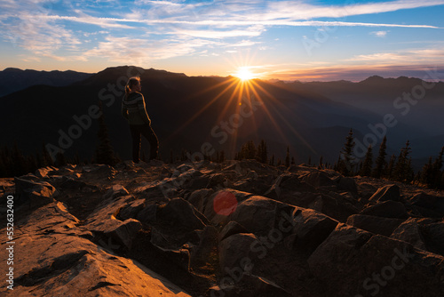 Woman looking out at sunset over Olympic mountains on mostly clear day from rocky mountain summit