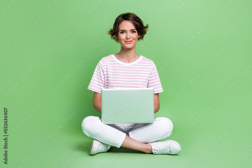 Full length photo of gorgeous young girl coding new software laptop working wear stylish striped garment isolated on green color background Full length photo of gorgeous young girl coding new software laptop working wear stylish striped garment isolated on green color background