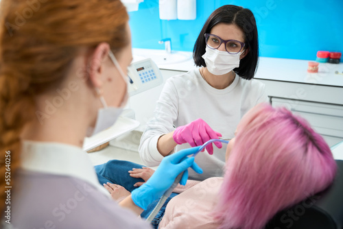 Woman orthodontist in glasses with assistant perform maintenance braces system