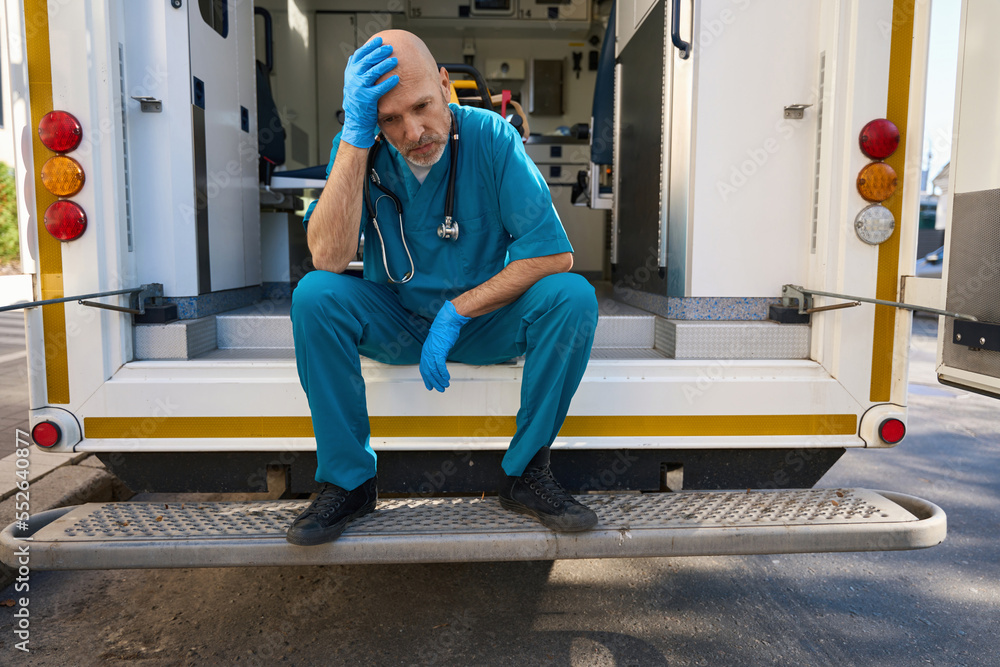 Doctor crouched while working on road and touches head with hand Doctor crouched while working on road and touches head with hand