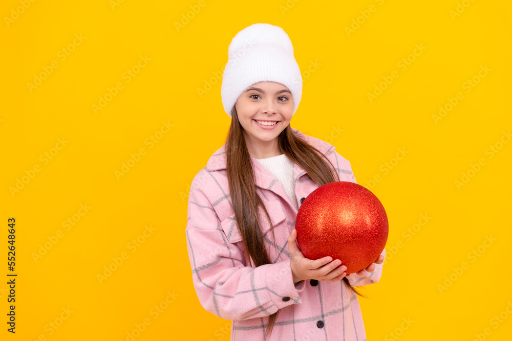 cheerful kid in winter hat hold christmas decorative ball on yellow background, christmas cheerful kid in winter hat hold christmas decorative ball on yellow background, christmas