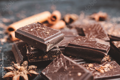 Dark chocolate bar pieces on dark background with grated chocolate and spices, pile chunks of broken chocolate
