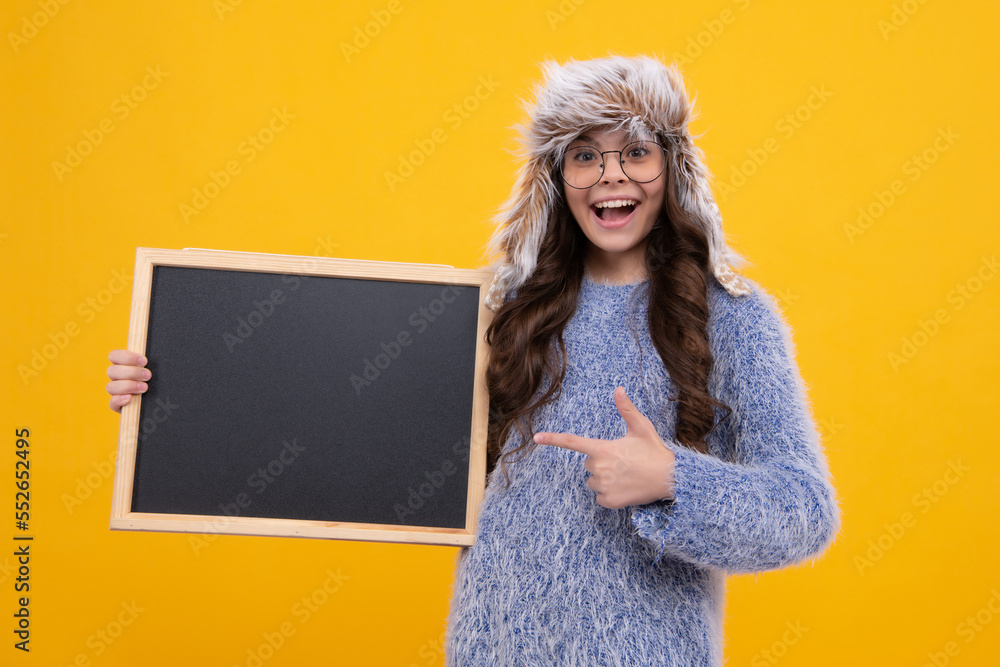 School sales board. Teen schoolgirl in warm winter hat hold blackboard. Back to school. Excited face, cheerful emotions of teenager girl. School sales board. Teen schoolgirl in warm winter hat hold blackboard. Back to school. Excited face, cheerful emotions of teenager girl.