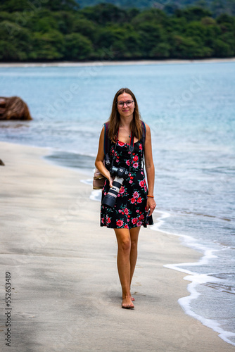 A beautiful backpacker girl with a camera walks on a tropical beach on the Caribbean coast of Costa Rica; beach vacation in Costa Rica