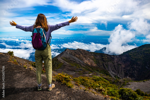 girl with backpack standing on top of volcano irazu in Costa Rica, volcanic landscape of Irazú Volcano National Park, massive volcano in clouds in Costa Rican mountains photo