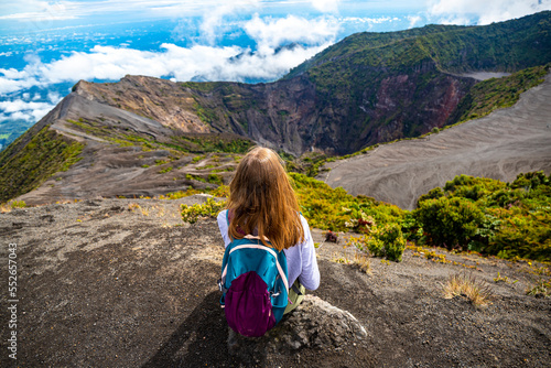 girl with backpack sits on top of volcano irazu in Costa Rica, volcanic landscape of Irazú Volcano National Park, massive volcano in clouds in Costa Rican mountains photo