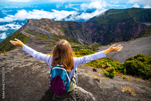 girl with backpack sits on top of volcano irazu in Costa Rica, volcanic landscape of Irazú Volcano National Park, massive volcano in clouds in Costa Rican mountains
