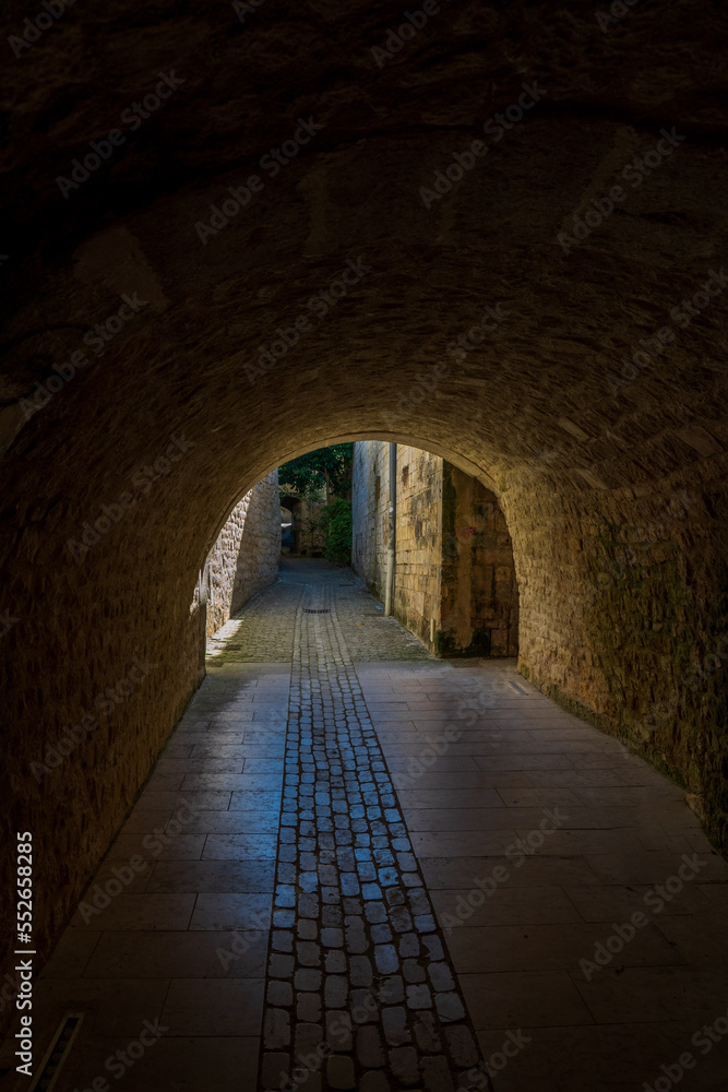 light in the tunnel. Medieval cobbled street, concrete wall and house
