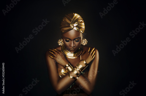 Photo Portrait closeup fantasy african woman face in gold paint. Golden shiny skin. Fashion model girl goddess hand fingers posing. Arab turban head, jewellery bracelets. metallic makeup. black studio