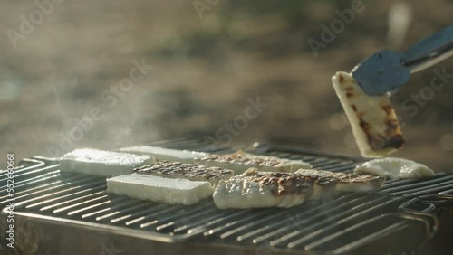 Fry Halloumi cheese on the grill. Picnic on the beach. I turn the pieces over with tongs photo