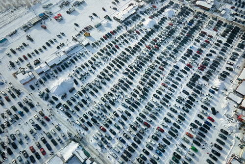 Aerial view of many cars parked for sale and people customers walking on car market or parking lot in winter